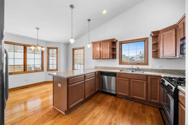 a kitchen with stainless steel appliances granite countertop wooden cabinets a sink dishwasher a stove and a refrigerator with wooden floor