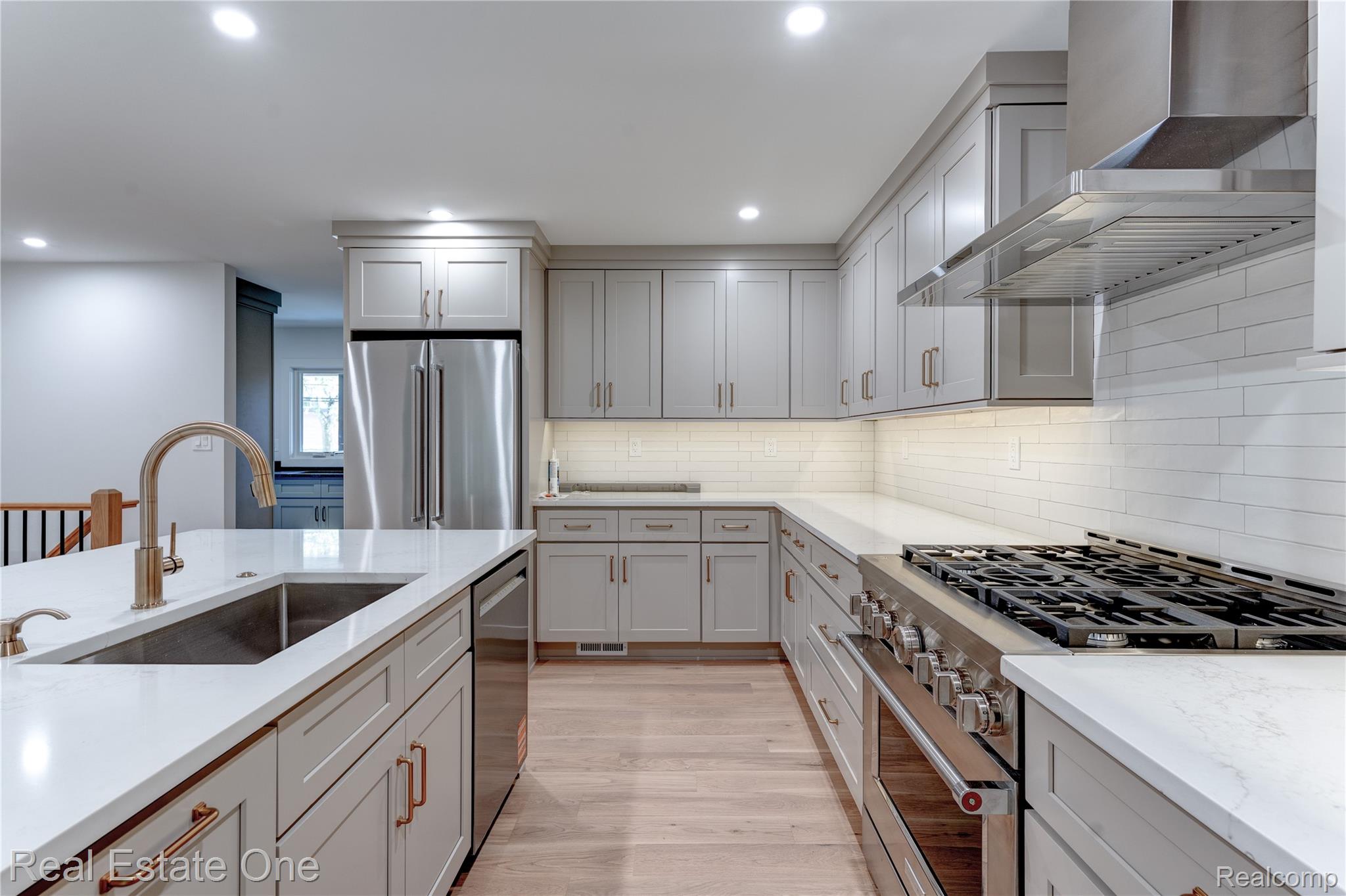 786 South Cranbrook Road Bloomfield Hills, MI 48301 - Photo 8 of 38 Kitchen with high end appliances, wall chimney range hood, light wood-style flooring, recessed lighting, and light stone counters