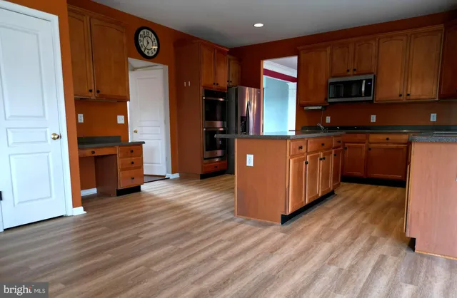 a kitchen with stainless steel appliances granite countertop wooden cabinets a refrigerator a stove a sink and dishwasher with wooden floor