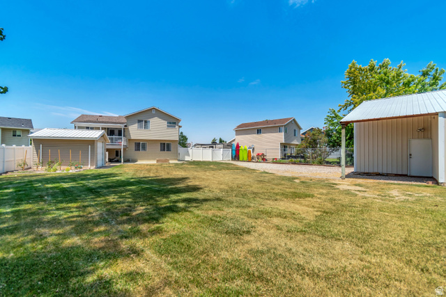 4752 South 4075th Street West Roy, UT 84067 - Photo 27 of 28 Expansive backyard featuring a large grassy area, a gravel parking area, and two separate storage sheds