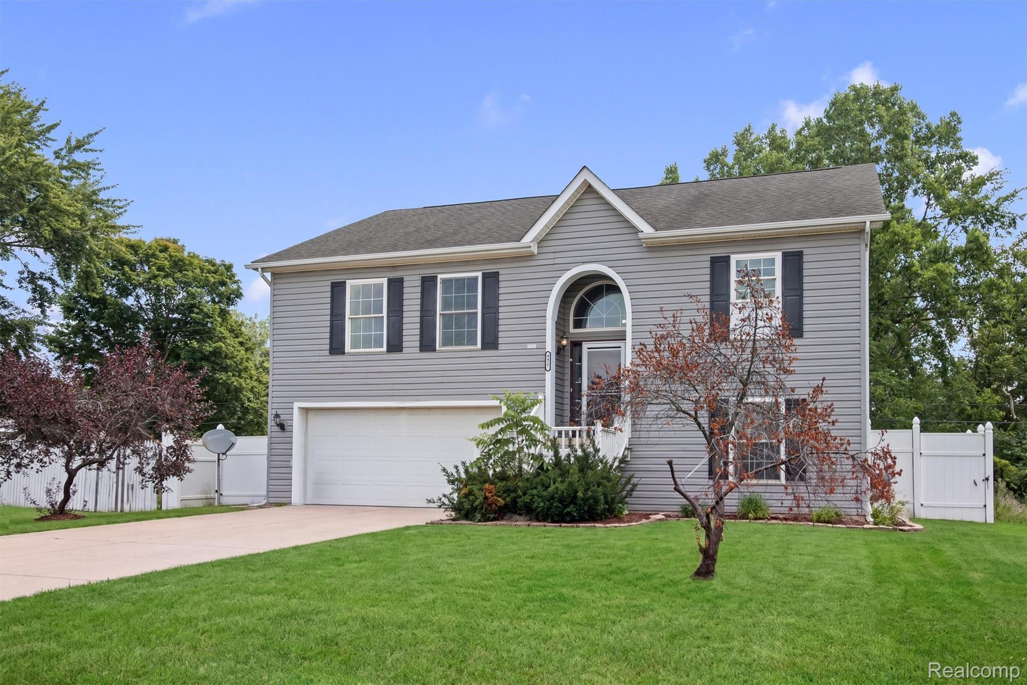 Split-level residence featuring gray siding, an arched entryway, a two-car garage, and a concrete driveway
