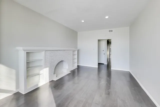 a view of an empty room with a fireplace and wooden floor