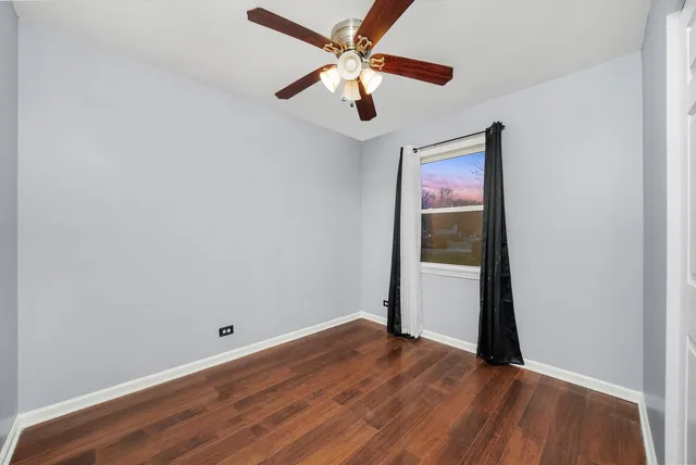 an empty room with wooden floor and a ceiling fan