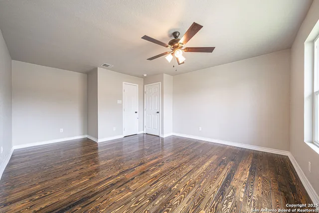 an empty room with wooden floor fan and windows