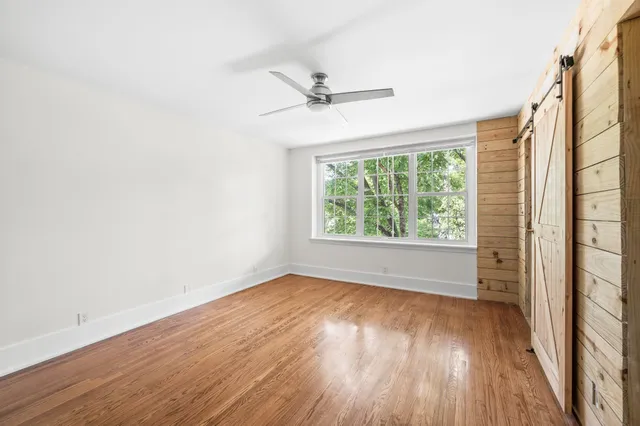 an empty room with wooden floor closet fan and windows