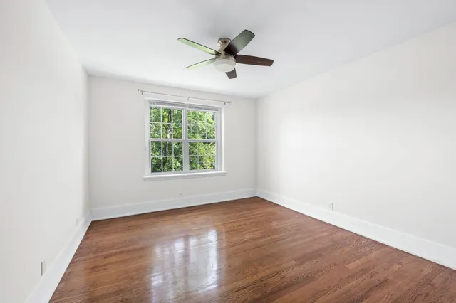 an empty room with wooden floor chandelier fan and windows