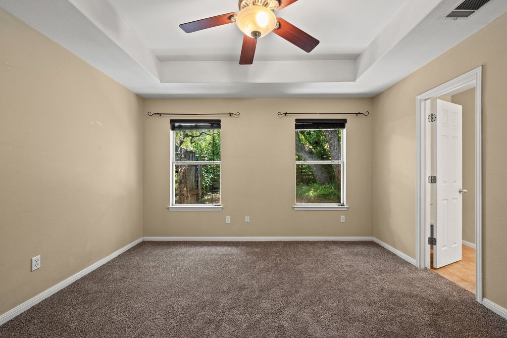 5208 Sioux Lane Austin, TX 78734 - Photo 21 of 35 A well-lit bedroom with a ceiling fan, plush carpeting, and two windows offering serene views.