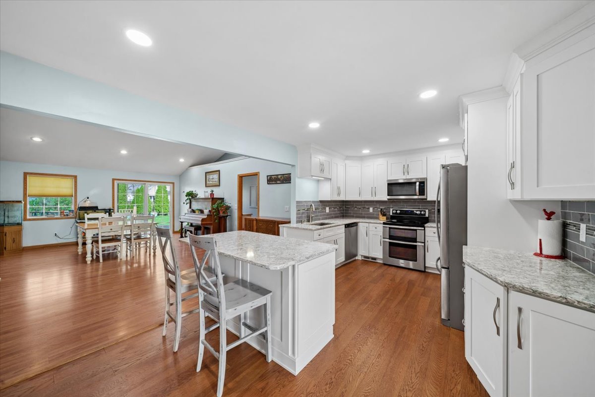 2 Division Street Bristol, IL 60512 - Photo 8 of 44 a kitchen with stainless steel appliances granite countertop a refrigerator a stove top oven and a dining table with wooden floor
