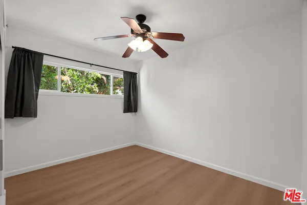 a view of empty room with wooden floor and fan