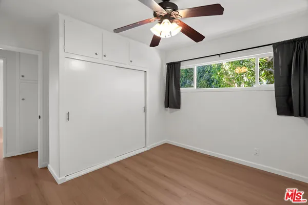 an empty room with wooden floor fan and windows