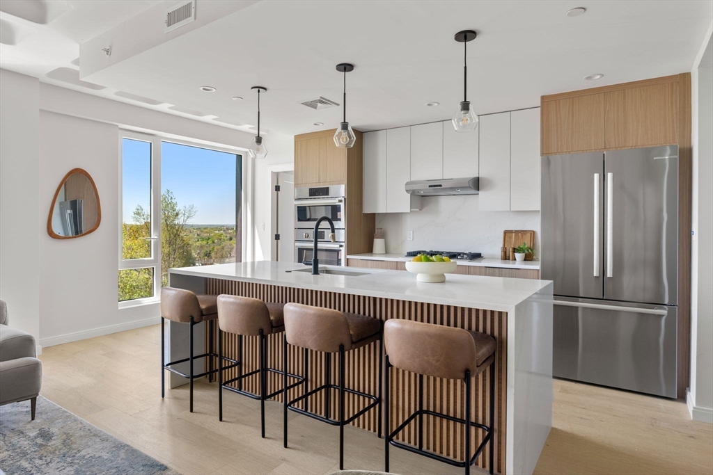 125 Lowell Street, Unit 402 Somerville, MA 02143 - Photo 6 of 34 a kitchen with stainless steel appliances granite countertop a dining table chairs refrigerator and cabinets
