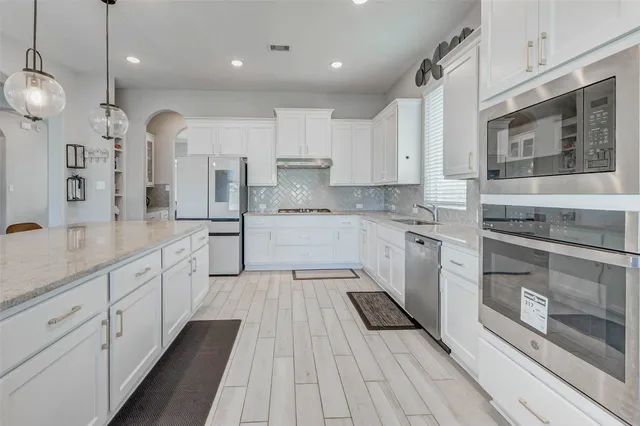 a large kitchen with stainless steel appliances kitchen island granite countertop a stove a sink a refrigerator and white cabinets with wooden floor