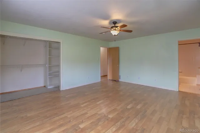 a view of an empty room with wooden floor and a ceiling fan