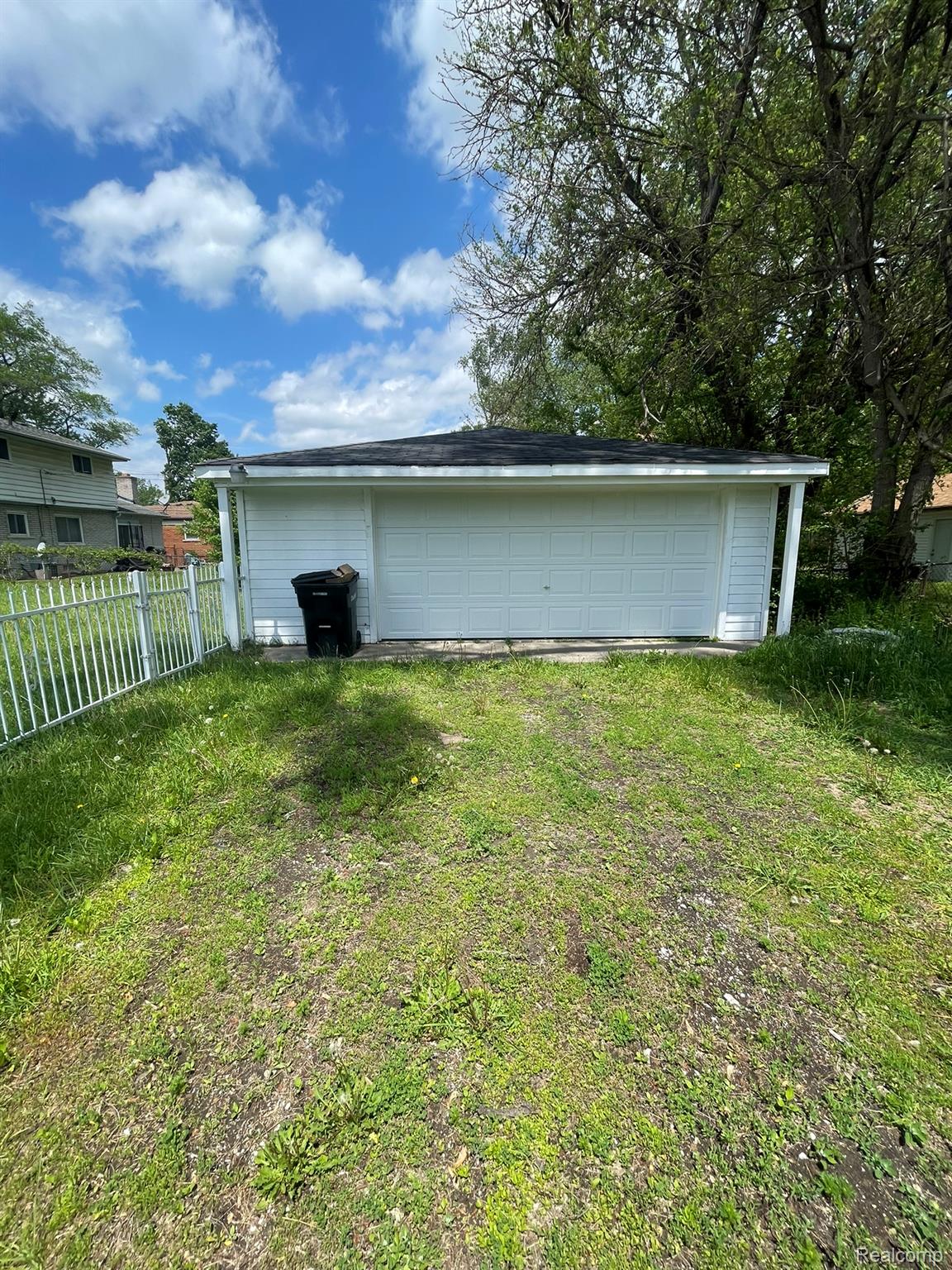 Detached white siding garage with a single overhead door, black shingle roof, and concrete apron