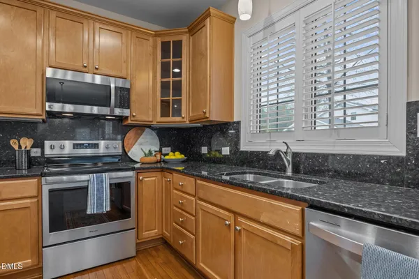 a kitchen with stainless steel appliances granite countertop wooden cabinets a refrigerator a sink a stove a microwave and wooden floors