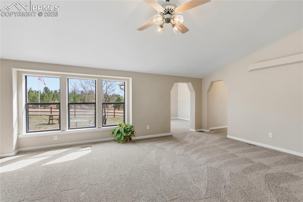 585 Mills Ranch Road Woodland Park, CO 80863 - Photo 20 of 46 Empty room with ceiling fan, arched walkways, light carpet, and vaulted ceiling