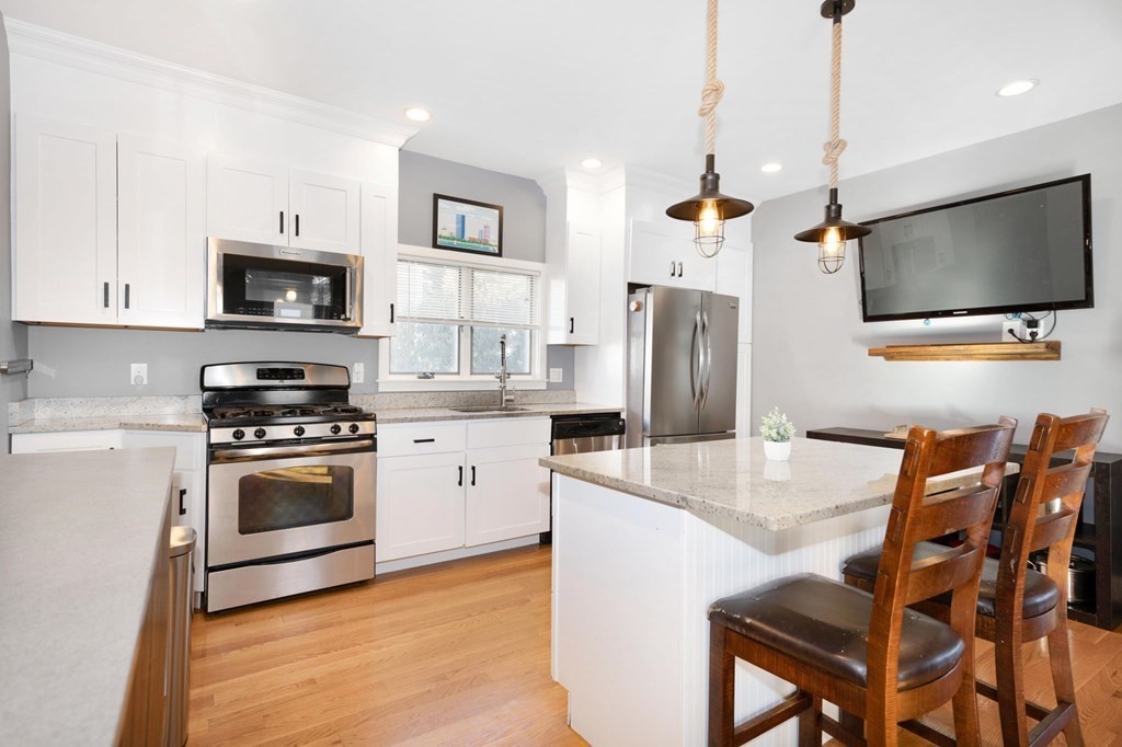 15 Vine Street Medford, MA 02155 - Photo 4 of 23 a kitchen with stainless steel appliances granite countertop a stove a refrigerator a microwave a sink a dining table and chairs with wooden floor