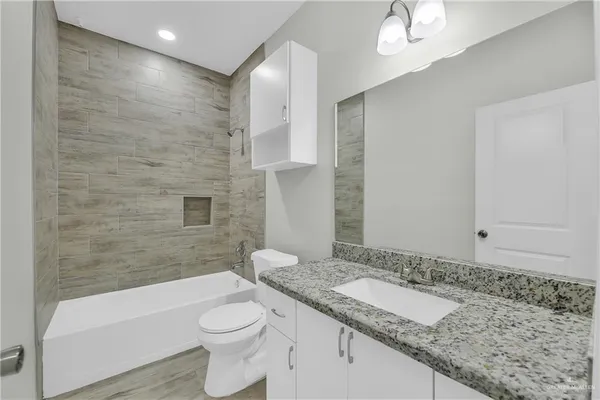 a bathroom with a granite countertop sink a toilet a mirror and bathtub