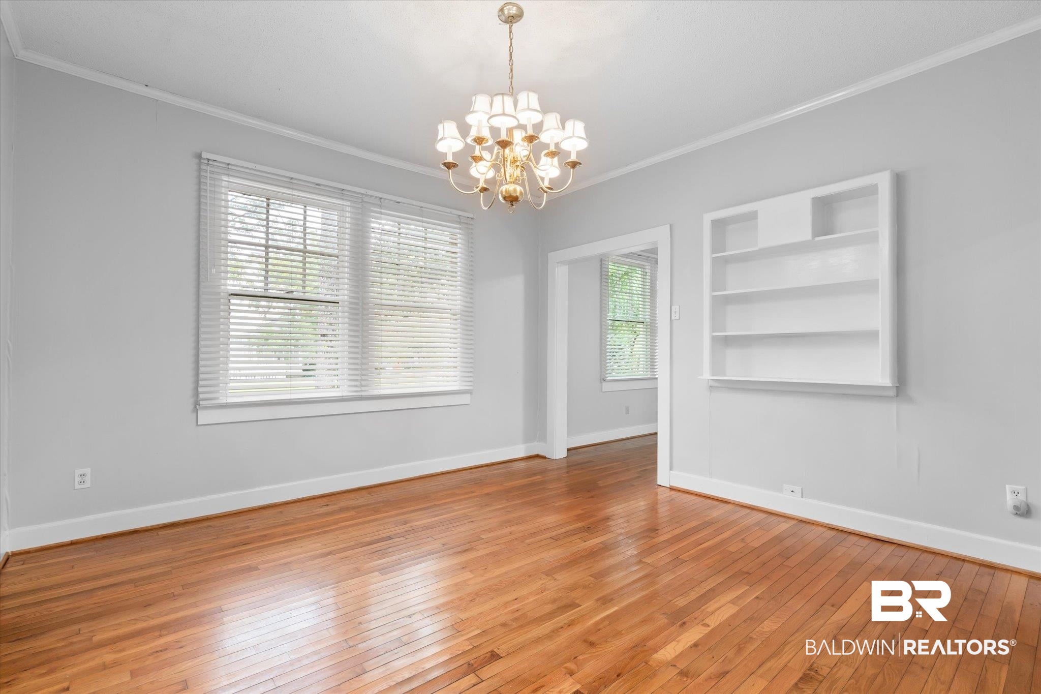 211 3rd Street Mobile, AL 36611 - Photo 6 of 20 Empty room with crown molding, built in shelves, an inviting chandelier, and hardwood / wood-style flooring