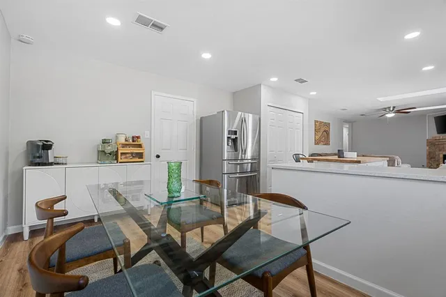 a kitchen with stainless steel appliances kitchen island granite countertop a dining table chairs and a refrigerator