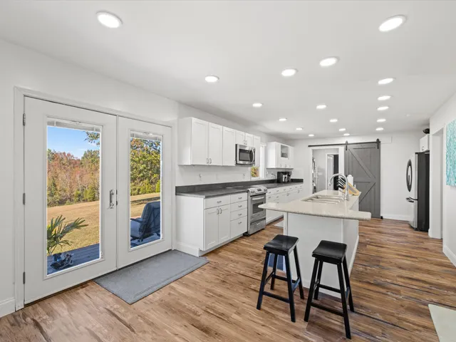 a large white kitchen with wooden floor and a large window