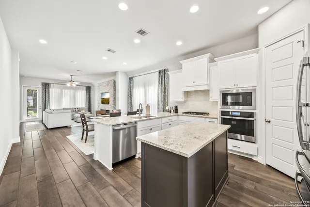 a large kitchen with a center island wooden floor and stainless steel appliances