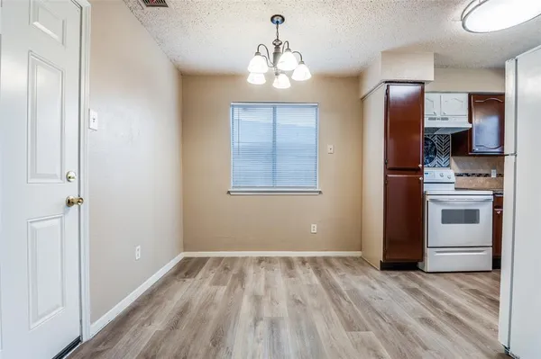 an empty room with wooden floor kitchen view and windows