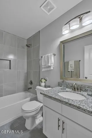 a bathroom with a granite countertop bathtub shower sink vanity mirror and toilet