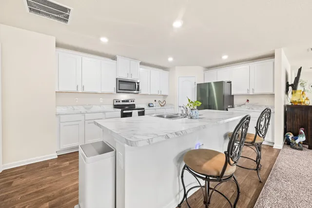 a kitchen with kitchen island granite countertop a stove a sink a oven a dining table and chairs with wooden floor