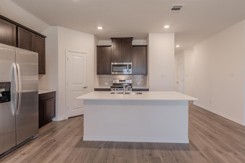 2902 Trusting Way Aubrey, TX 76227 - Photo 9 of 38 Kitchen featuring a large central island, stainless steel appliances, dark wood cabinetry, light countertops, and wood-finish flooring
