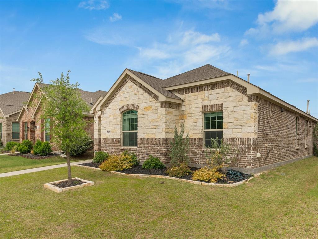 16936 Post Cedar Drive Justin, TX 76247 - Photo 28 of 30 Exterior featuring a blend of light-colored stone and brick facades, arched window accents, a neatly manicured lawn, and planted landscaping beds