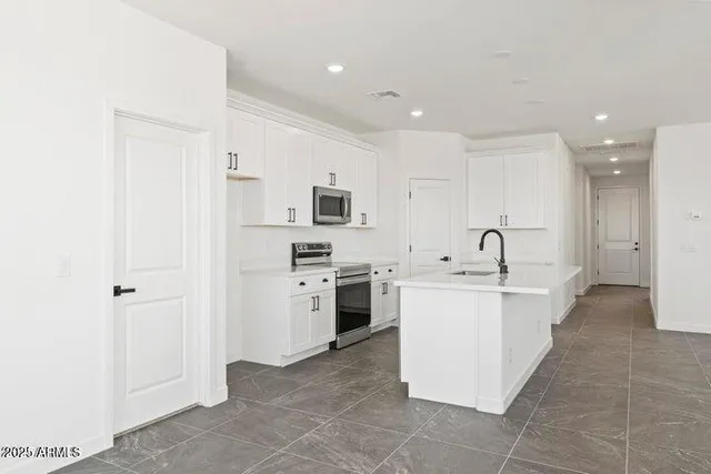 a large white kitchen with stainless steel appliances a sink a stove and a refrigerator