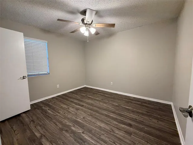 a view of an empty room with wooden floor and a chandelier fan