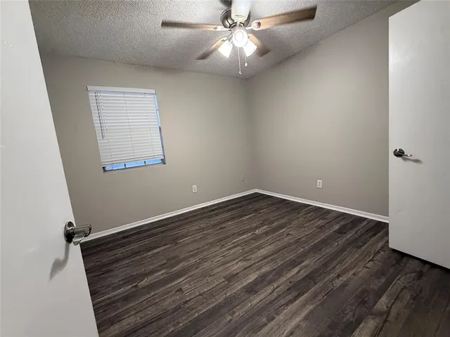an empty room with wooden floor chandelier fan and windows