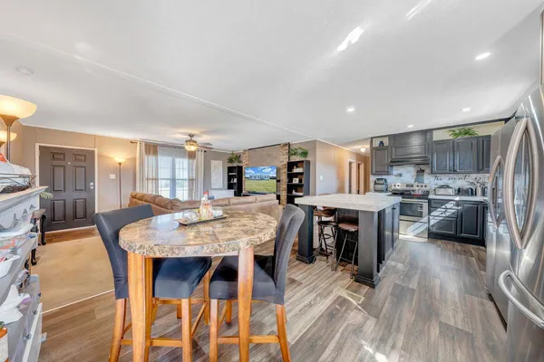 a dining room with stainless steel appliances kitchen island granite countertop a table chairs and a refrigerator