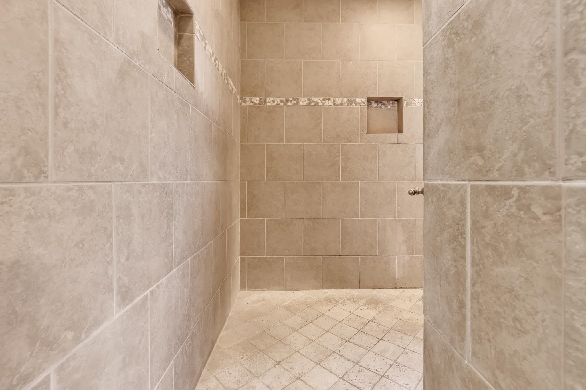 649 Ridge Springs Road Collierville, TN 38017 - Photo 26 of 38 Shower enclosure featuring large format neutral-toned wall tiles, a decorative mosaic tile accent band, two recessed wall niches, and a textured tile floor