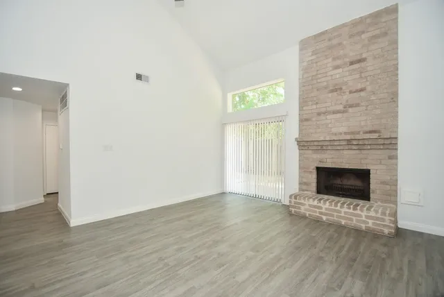 an empty room with wooden floor fire place and windows