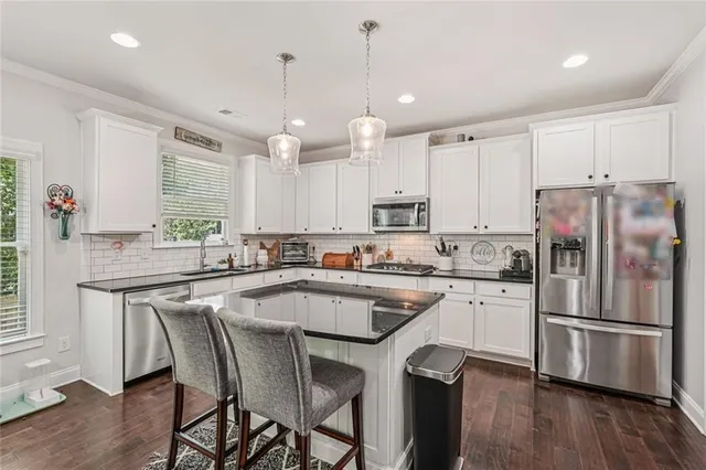 a kitchen with stainless steel appliances granite countertop a refrigerator a sink dishwasher a stove and white cabinets with wooden floor