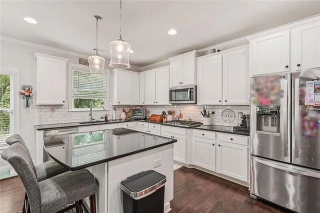 a kitchen with stainless steel appliances granite countertop a sink a stove a refrigerator cabinets and chairs