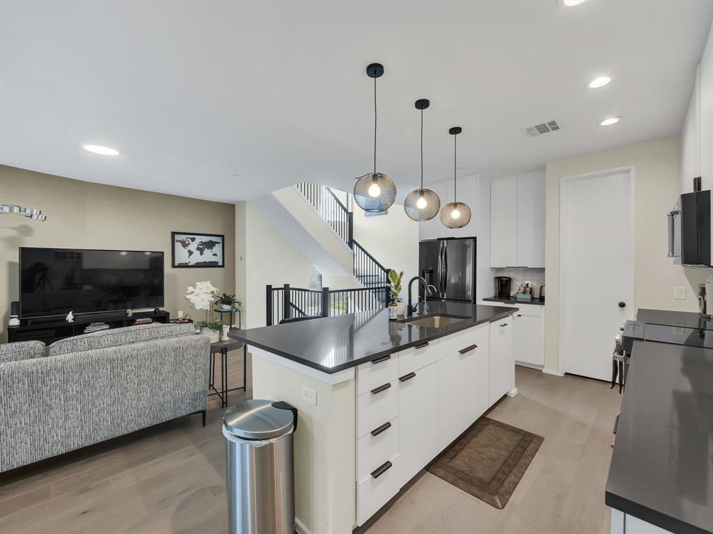 a kitchen with granite countertop a sink a microwave oven a stove and a refrigerator with wooden floor