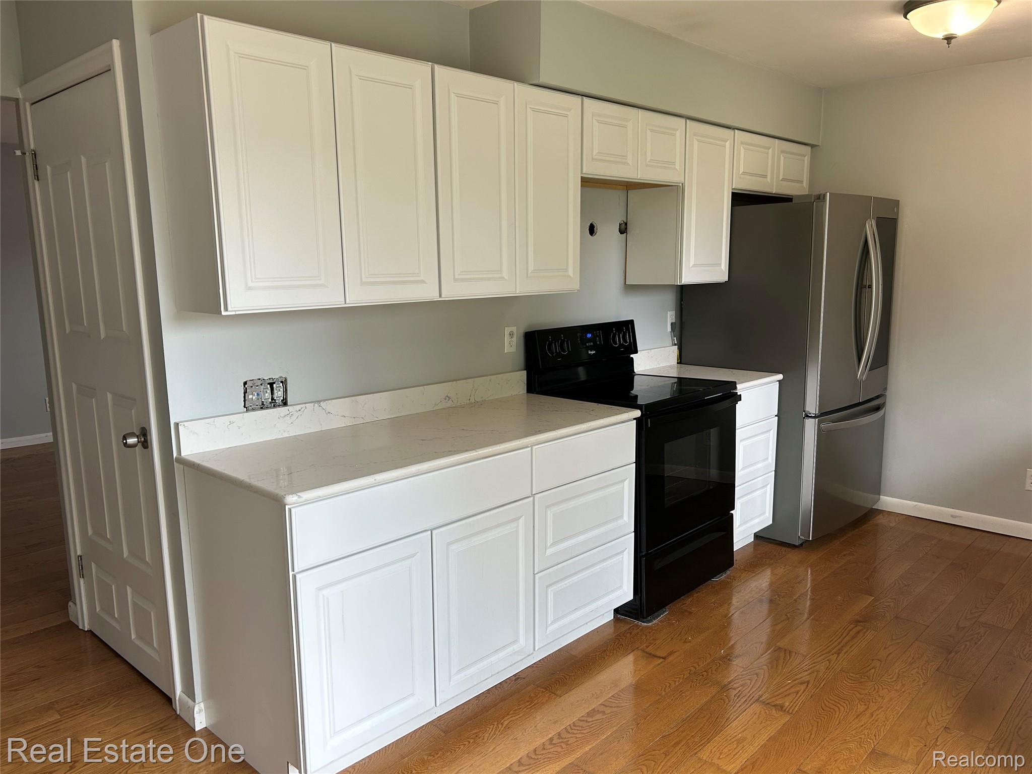 2659 Benstein Road Commerce Township, MI 48382 - Photo 4 of 26 Kitchen area featuring white shaker-style cabinetry, light-toned countertops, a black electric range, a stainless steel refrigerator, and wood-finish flooring