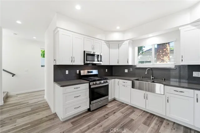 a kitchen with stainless steel appliances white cabinets a sink a stove a microwave and wooden floors