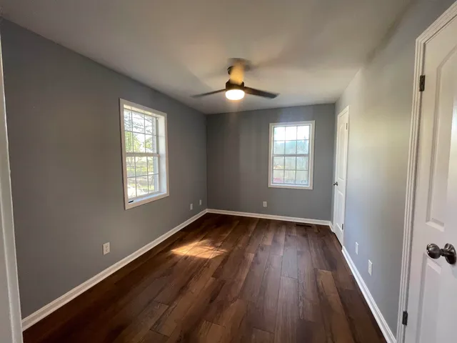 an empty room with wooden floor chandelier fan and windows