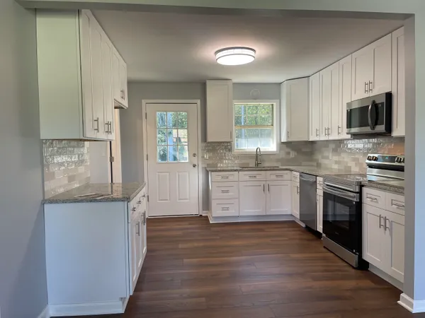 a kitchen with stainless steel appliances granite countertop a stove top oven a sink dishwasher and a refrigerator with wooden floor