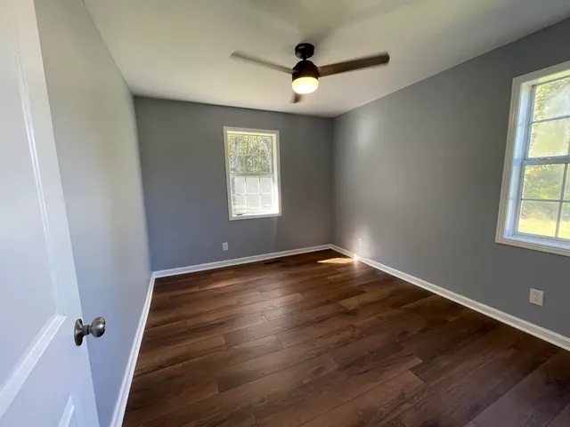 an empty room with wooden floor fan and windows