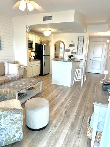 a living room with kitchen island stainless steel appliances furniture a rug kitchen view and a table