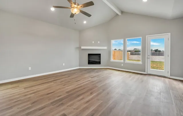 a view of an empty room with wooden floor and a ceiling fan