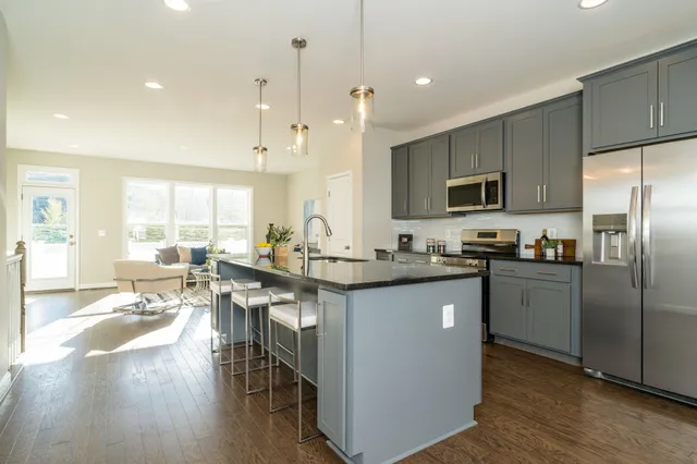 a kitchen with stainless steel appliances granite countertop a refrigerator a stove top oven a sink dishwasher a dining table and chairs with wooden floor