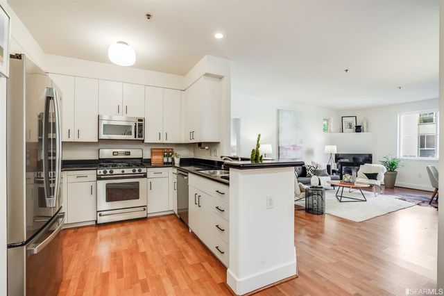 a kitchen with stainless steel appliances granite countertop a stove top oven a sink dishwasher and a refrigerator with wooden floor