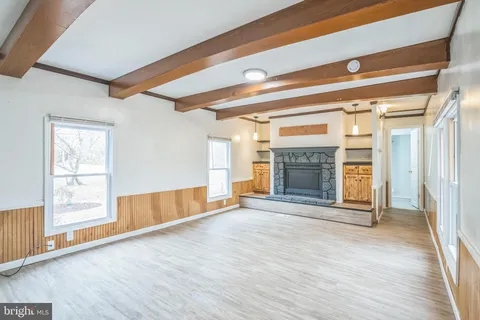 a view of an empty room with wooden floor fireplace and a window